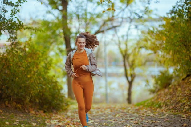 Eine junge Frau läuft durch einen herbstlichen Wald, wobei ihr zu einem Pferdeschwanz zusammengebundenes Haar in der Luft wehlt