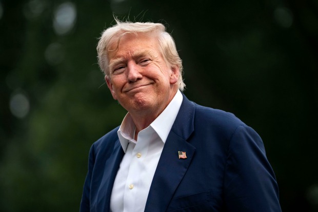 Donald Trump in dunkelblauem Anzug mit US-Flaggen-Pin, lächelnd.
