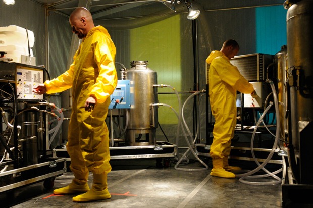Bryan Cranston als Walter White und Aaron Paul als Jesse Pinkman in gelben Schutzanzügen zwischen Laborgeräten und Chemiebehältern in einer Szene aus „Breaking Bad“.