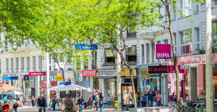 Radfahrer und Passanten auf einer belebten Einkaufsstraße, verschiedene Shops