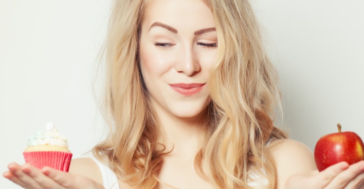 Junge blonde Frau hält in der einen Hand Cupcake, in der anderen Apfel