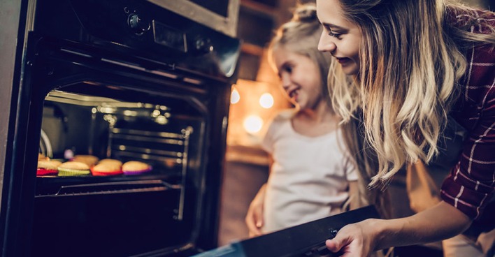 Junge Mutter öffnet Backrohr, um nach den Muffins zu sehen | Credit: iStock.com/Vasyl Dolmatov