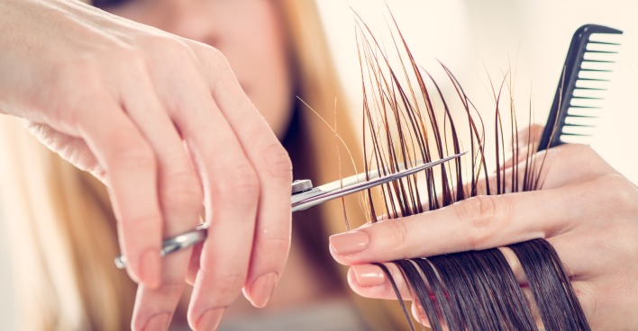 Eine Friseurin unscharf im Hintergrund, im Vordergrund ihre Hände beim Schneiden