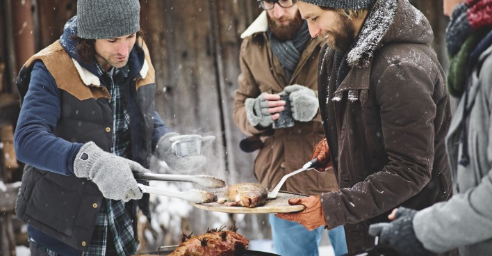 Vier Männer stehen in dicker Wintermontur rund um einen Griller im Freien