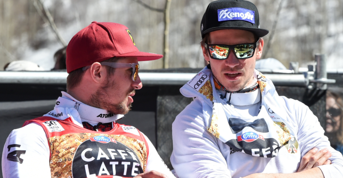 Marcel Hirscher und Felix Neureuther, die in Rennanzügen sowie mit Sonnenbrillen und Schirmmützen bekleidet, auf Stühlen sitzend miteinander diskutieren