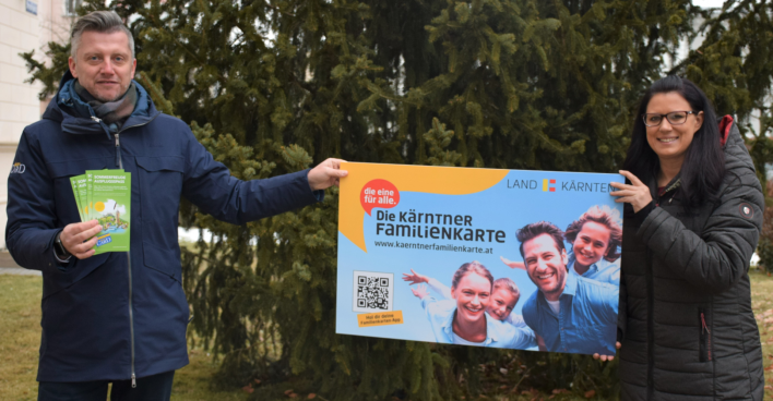 Sara Schaar und Anton Fasching halten vor einem Baum im Garten der Landesregierung das überdimensional große Modell einer Kärnten Card in die Höhe