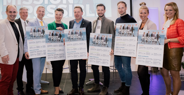 Vertreter der JW-Kärnten übergeben den Spitzenkandidaten der Parteien der kommenden Landtagswahl auf einer Diskussionsbühne jeweils eine überdimensionierte Forderungsliste