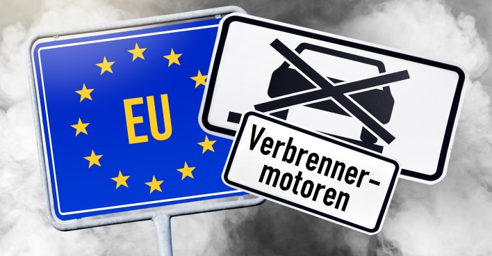 Ein EU-Ortsschild, ein Autoverbotsschild und die Aufschrift "Verbrenner-Motoren" vor dem Hintergrund von Autoabgasen