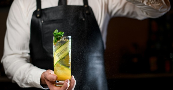 Barkeeper hält einen Cocktail mit einer langen Gurkenscheibe | Credit: istock.com/MaximFesenko