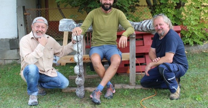 Drei Bildhauer, sitzend und kniend, lächeln in die Kamera.
