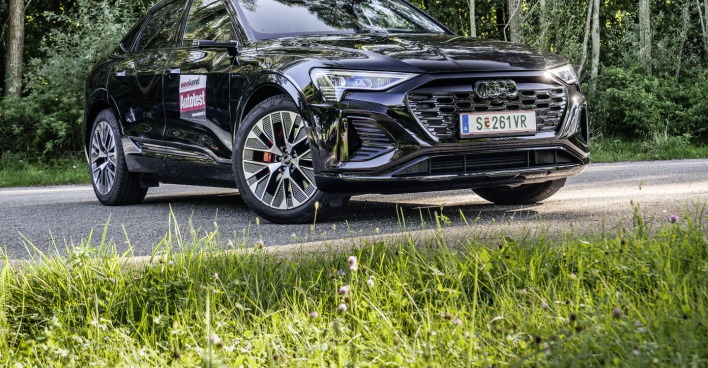 Der Audi Q8 e-tron Sportback frontal von vorne auf einer Straße, die durch einen Wald führt