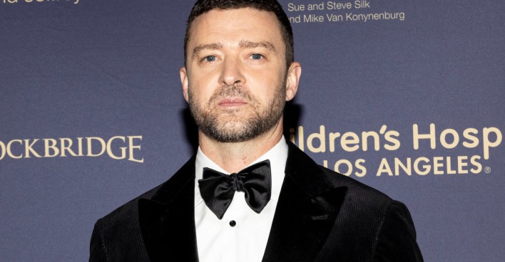Justin Timberlake trägt einen schwarzen Suite und kurze Haare vor einer Fotoleinwand.