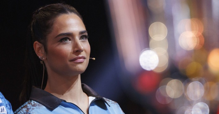 Amira Pocher in einem hellblauen Sportshirt. Sie sieht in die Ferne und hat ein Mikrofon an ihrer Wange montiert.