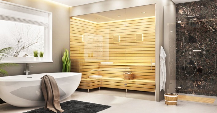 Ein Badezimmer mit einer weißen freistehenden Badewanne, einer Dusche mit dunklen Wandfliesen und eine moderne Sauna im Holzstil, die mittels Glasfront vom restlichen Raum abgetrennt ist.