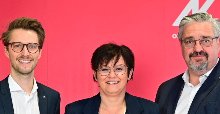 In der Mitte lacht eine Dame mit kurzen braunen Haaren. Ebenfalls lachend: Die Herren links und rechts von ihr, die beiden einen kurzen Vollbart haben und eine Brille tragen. Zu sehen sind links: Gerhard Bremm (Wahlleiter), Andrea Heimberger (AK-Direktorin) und Andreas Stangl (AK-Präsident)-