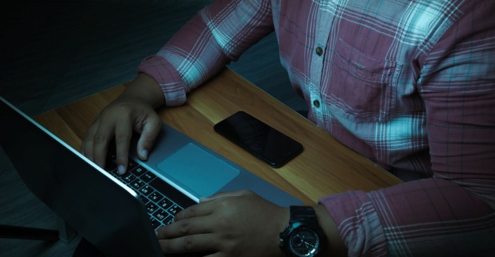 Ein Mann sitzt im Dunkeln vor einem Laptop.