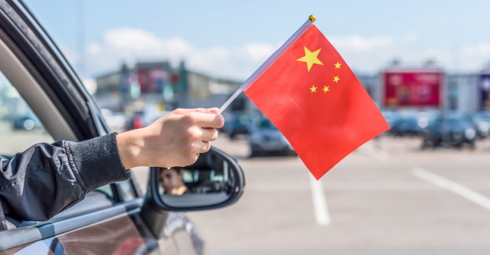 Hand hält chinesische Fahne aus dem Autofenster