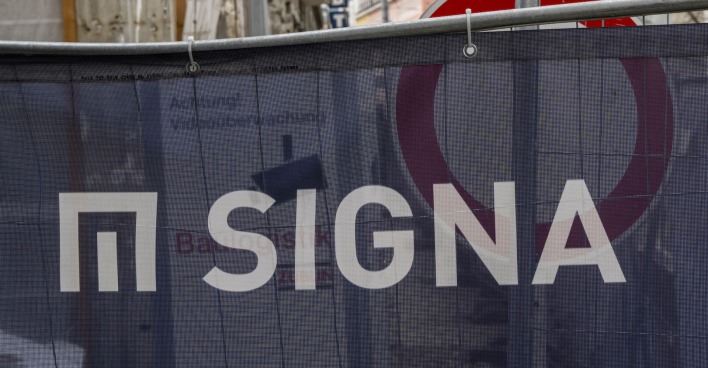 Eine Bauplane mit Logo und Schriftzug der Signa, dahinter ein Stoppschild