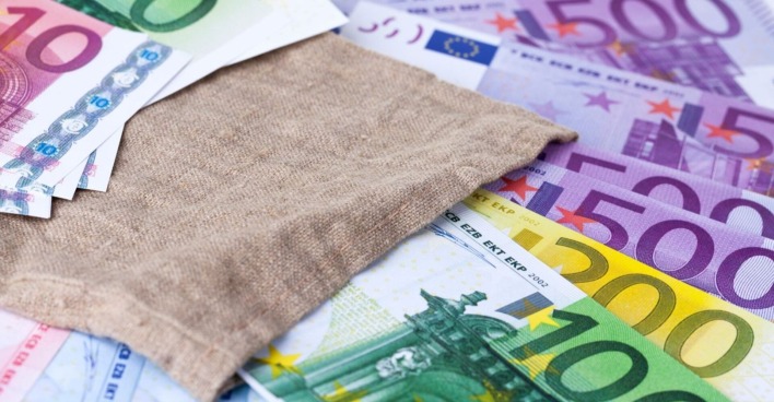 Euro-Noten auf einem Tisch, darüber ein Jutesack.