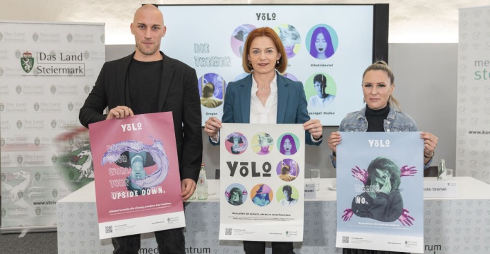 Mann und zwei Frauen stehen nebeneinander und präsenteren Plakate