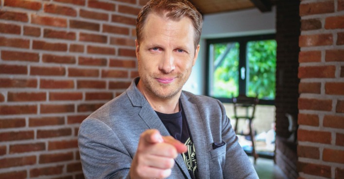Oliver Pocher mit einem grauen Anzug. Er zeigt in die Kamera.