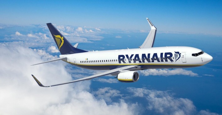 Ein weißes Flugzeug mit der blauen Aufschrift Ryanair schwebt über weißen Wolken und dem blauen Himmel.