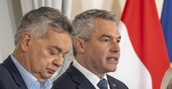 Werner Kogler und Karl Nehammer bei einer Pressekonferenz, im Hintergrund die Flagge Österreichs