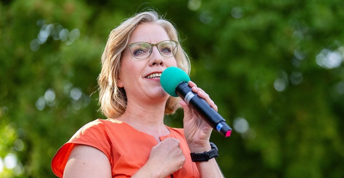 Leonore Gewessler mit Mikrofon auf einer Bühne.