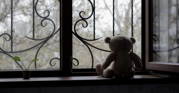 Ein Teddybär sitzt an einem einsamen, vergitterten Fenster.