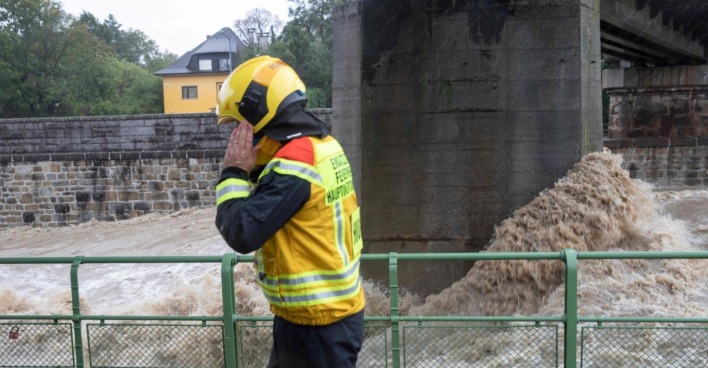 Ein Feuerwehrmann telefoniert, hinter ihm der reißende Wienfluss