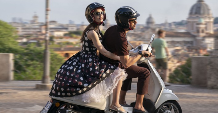 Frau fährt mit einem Mann gemeinsam auf einer Vespa durch eine Stadt