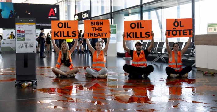 Vier Klimaaktivisten mit Protestschildern und verschütteter Farbe.