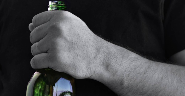 Nahaufnahme einer Hand, die den Hals einer Bierflasche umklammert