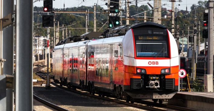 ÖBB-Zug auf der Stammstrecke in Wien, im Bereich eines Bahnhofs mit Signalanlagen und Gleisen im Vordergrund.