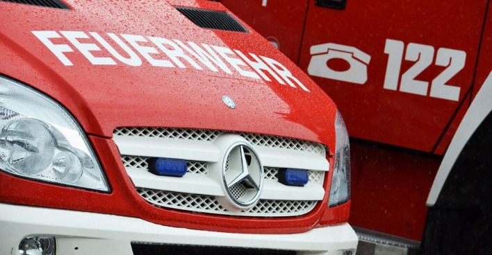 Nahaufnahme eines roten Feuerwehrfahrzeugs mit der Aufschrift „FEUERWEHR“ und der Notrufnummer 122, bei Regen fotografiert.
