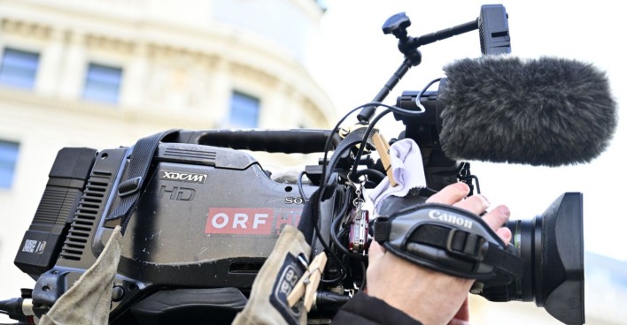 Nahaufnahme einer professionellen ORF-Fernsehkamera mit Mikrofon und Handgriff während eines Außendrehs.