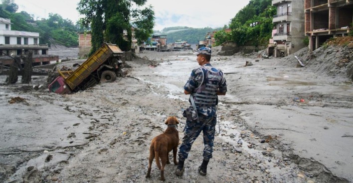 Sturzflut in Nepal: Sicherheitsbeamter mit Hund in einem von Schlamm und Trümmern verwüsteten Ort.