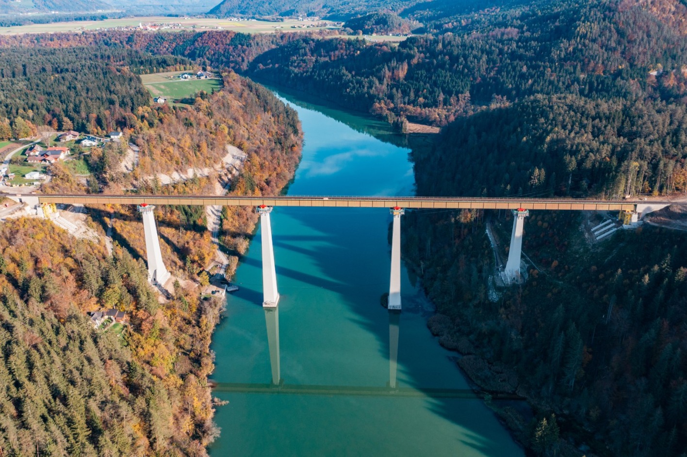 Die Jauntalbrücke, inmitten einer herbstlichen Waldlandschaft, unter der ein grünlich schimmernder Fluß verläuft