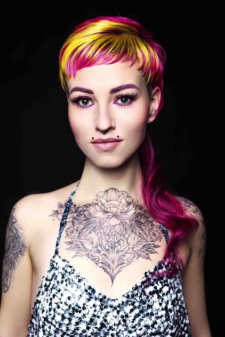 Eine Frau mit pink-gelben Haaren und Tattoos schaut direkt in die Kamera
