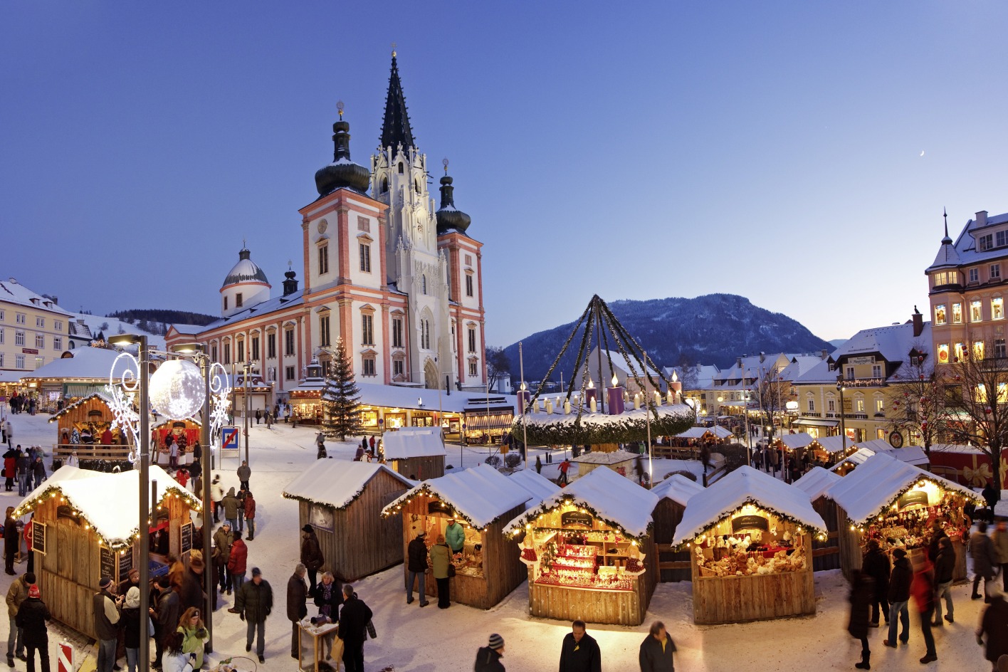 Ein Adventmarkt beim Sonnenuntergang, dahinter eine Basilika