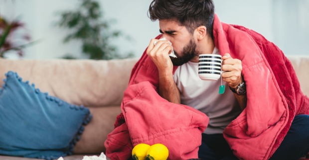 Mann kuriert Erkältung auf Sofa mit Hausmitteln