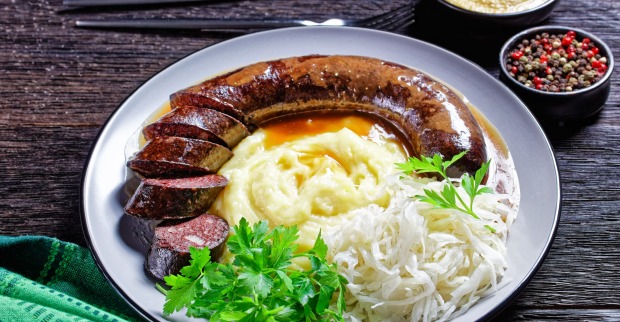 Eine gebratene Blutwurst mit Kartoffelpüree und Sauerkraut auf einem Teller mit Salatgarnierung