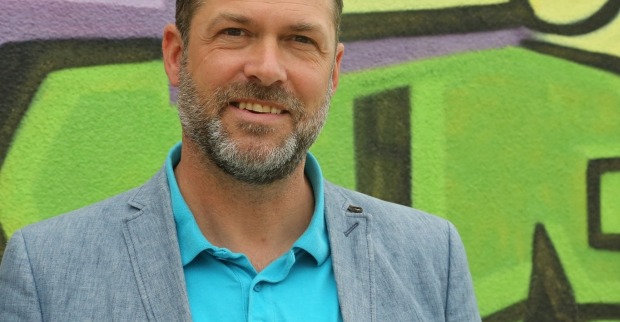 Stadtrat Markus Geiger steht vor einer mit Graffiti bemalten Wand.