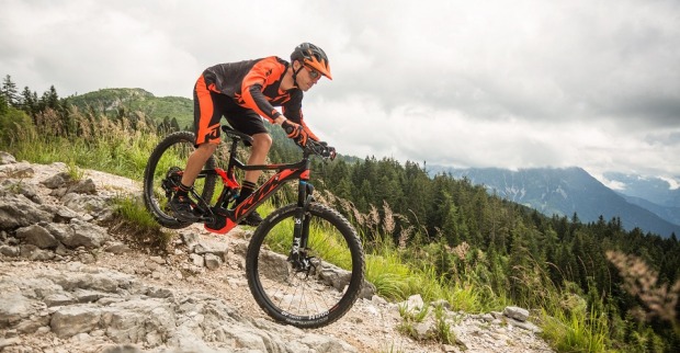 Mann mit Helm und Fahrradtrikot fährt mit einem E-Bike von KTM einen felsigen Berg hinunter.