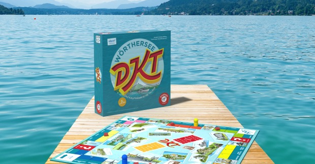 Ein Badesteg, der in einen türkisfarbenen See vor einer imposanten Bergkulisse ragt, auf dem ein DKT-Spielbrett platziert wurde