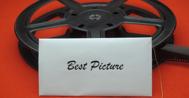 Eine schwarze Filmrolle auf einem roten Teppich an die ein weißer Briefumschlag mit der Beschriftung Best Picture angelehnt ist