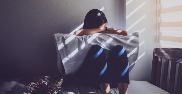 Depressive Frau mit Polster im Bett hockend