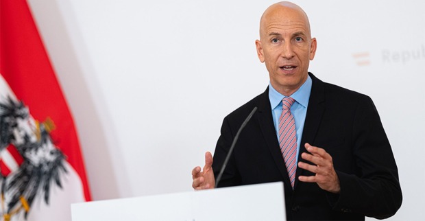 Kocher erklärt bei der Pressekonferent mit österreichischer Fahne im Hintergrund, die neuen Arbeitsmodelle