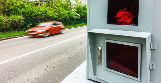 Ein oranges Auto fährt in hohem Tempo an einer Radarfalle vorbei
