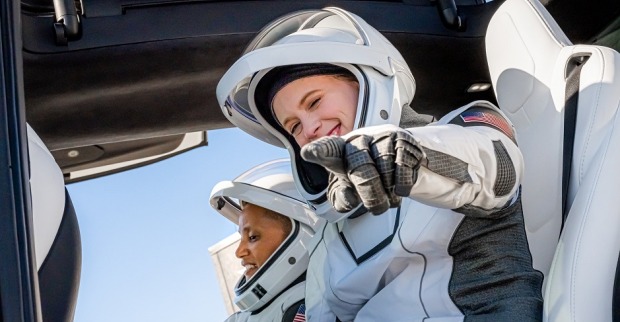 Zwei Frauen in Raumanzügen sitzen gut gelaunt und aufgekratzt in einem Tesla